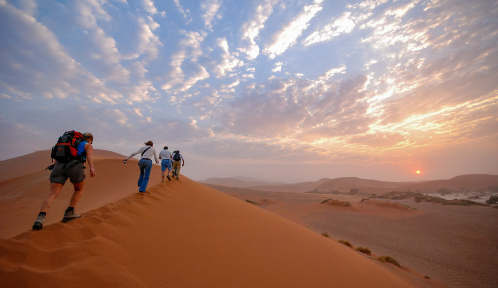 Wanderer auf einer roten Sandd&uuml;ne in der aufgehenden Sonne