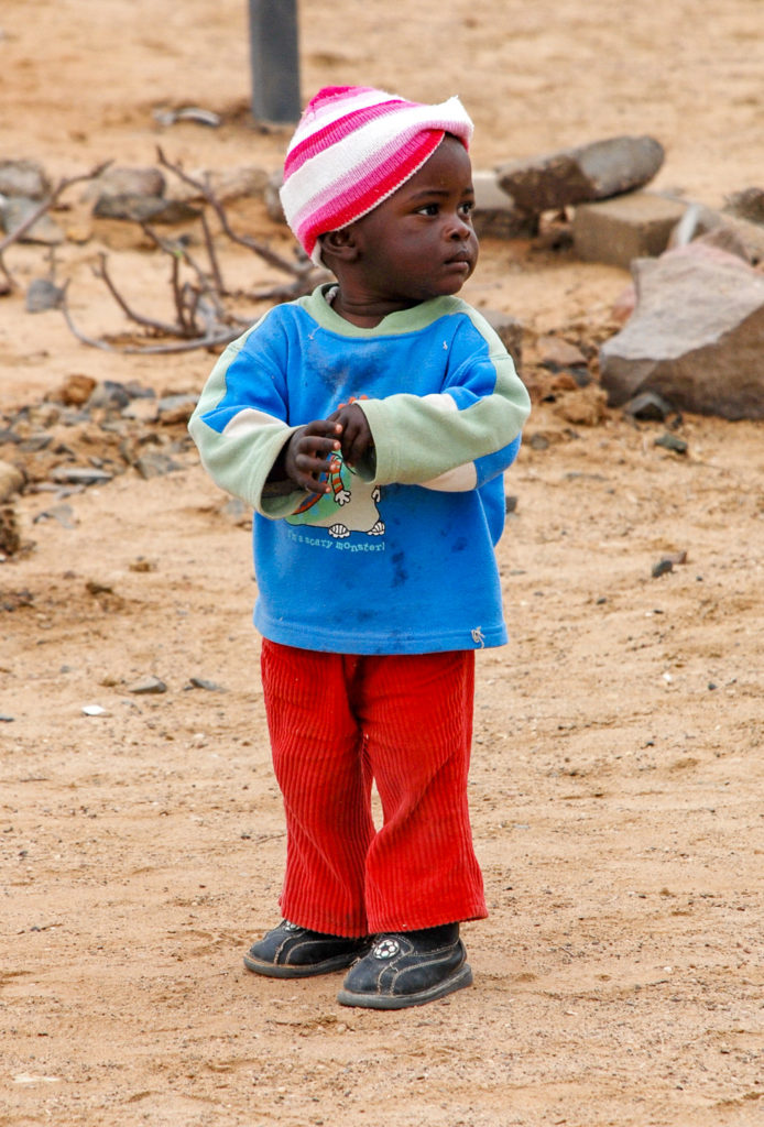 kleiner afrikanischer Junge mit roten Hosen und blauem Pullover