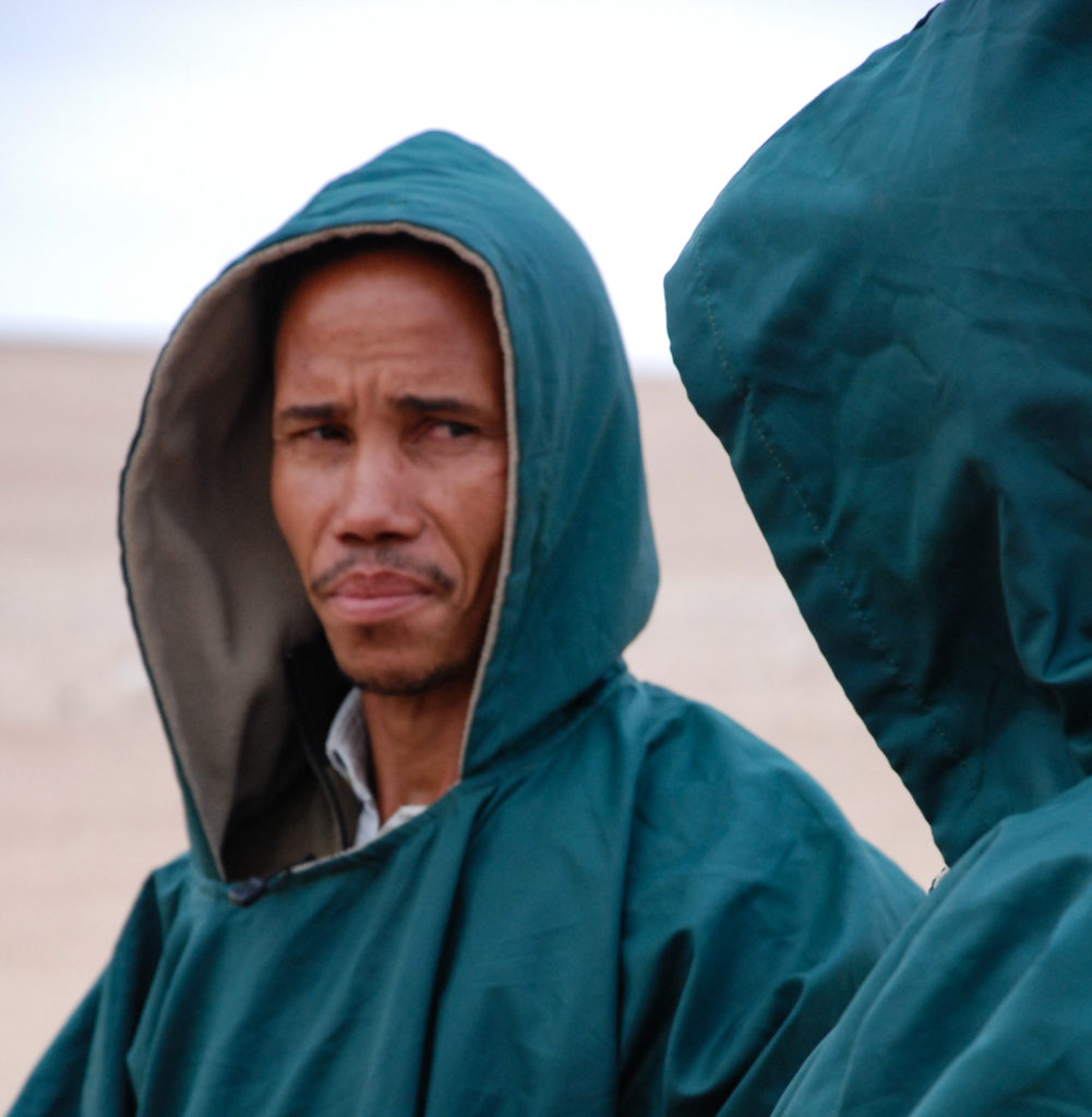 namibische Guides sch&uuml;tzen sich mit Kapuzen vor dem herumwirbelnden Sand