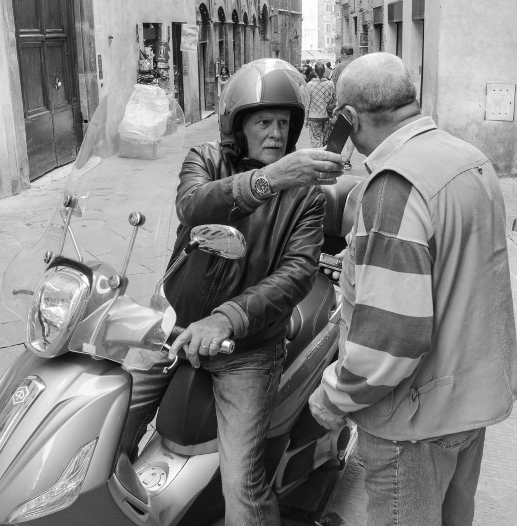 zwei ältere Italiener mit Handy und Vespa in schwarz-weiss