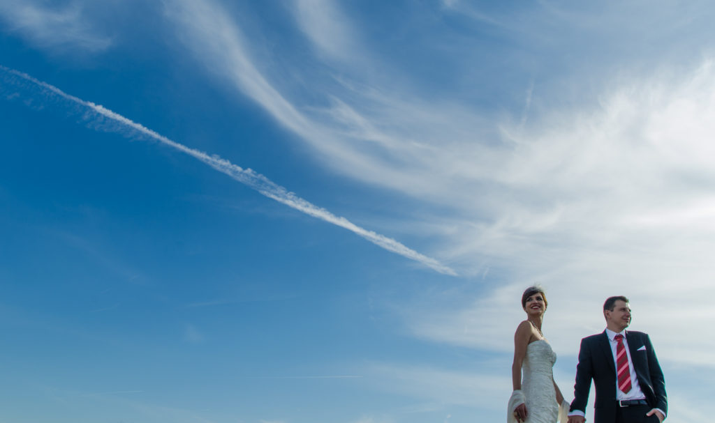 Hochzeitspaar vor leicht bew&ouml;lktem Himmel und Flugstreifen