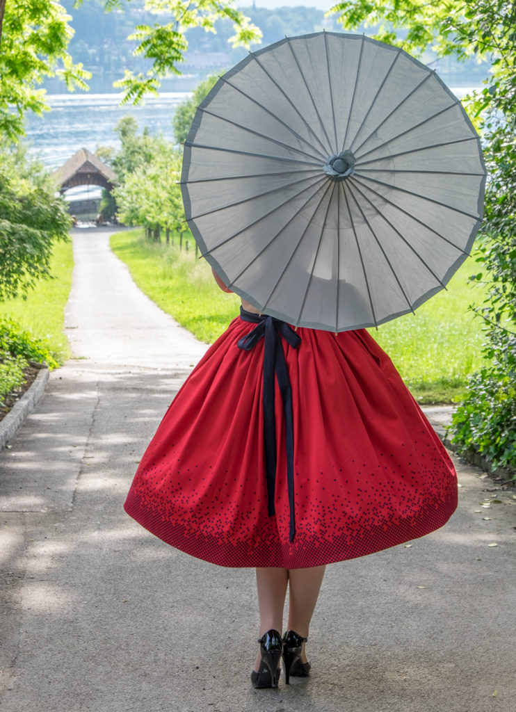 Modefotografie mit rotem Rock und Seidenschirm von hinten im Park