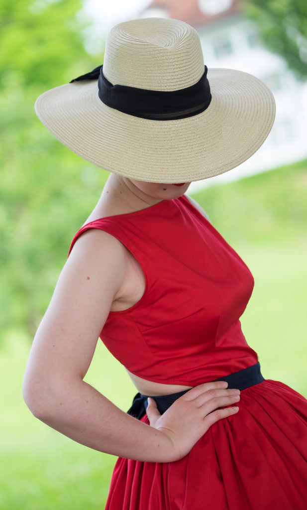 Modefotografie, weiblicher Torso im roten Kleid, das Gesicht durch einen Hut verdeckt