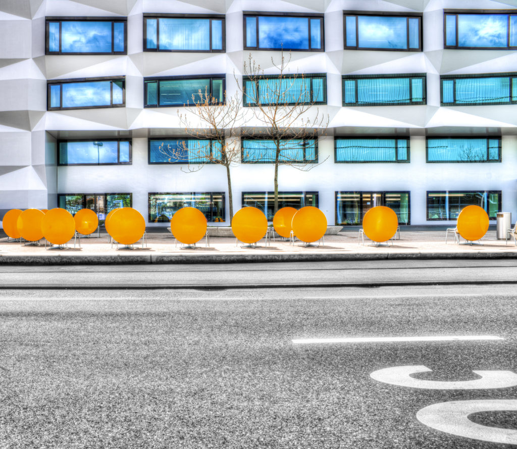 Fassade der Hochschule Luzern mit blauen Fenstern und orangen, runden Tischen