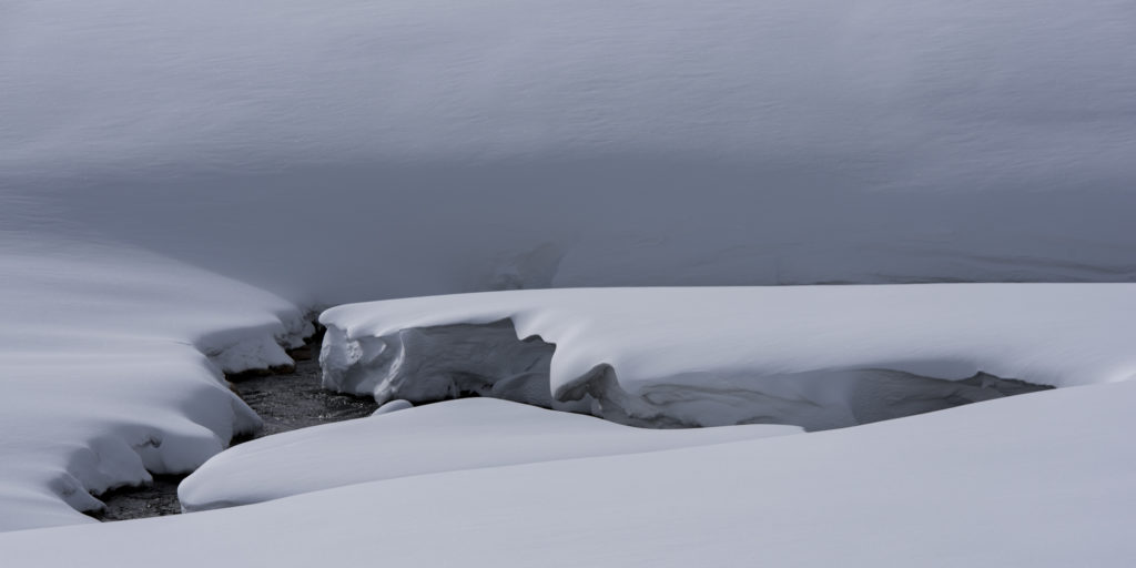 Flusslauf tief im Schnee eingeschnittener Bachlauf im winterlichen Licht