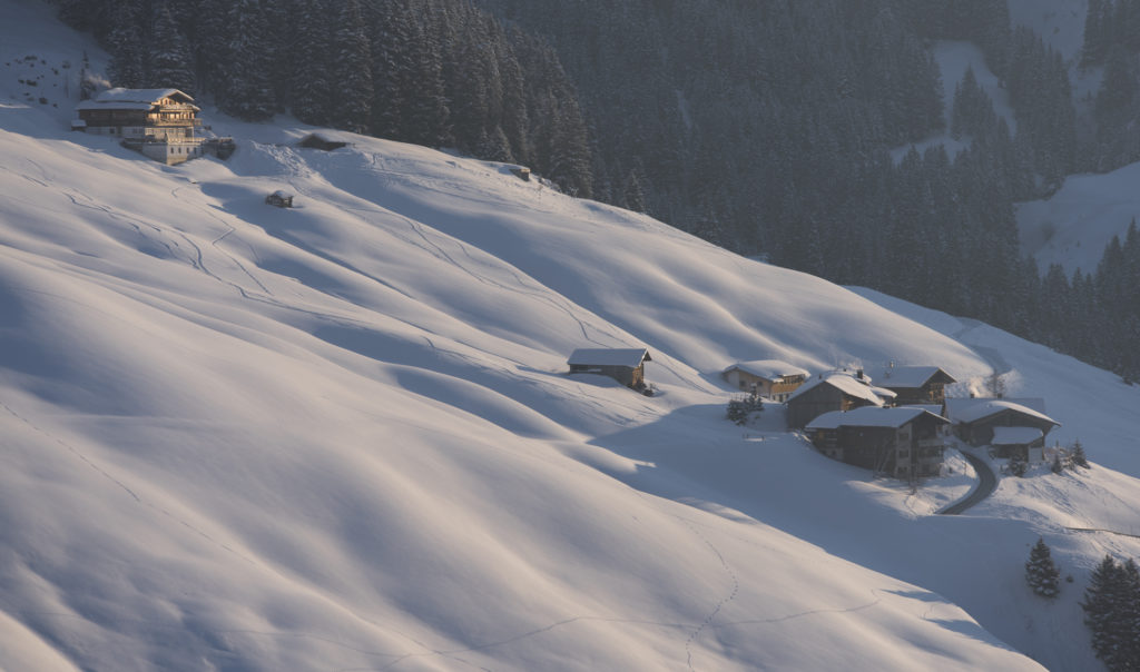 letzte Sonnenstrahlen kleiner Weiler am verschneiten Berghang im rötlichen Abendlicht