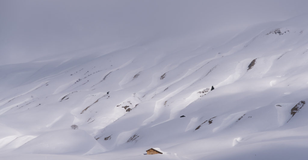 eingeschneit einsame, eingeschneite Alphütte, die Sonne durch den Nebel brechend