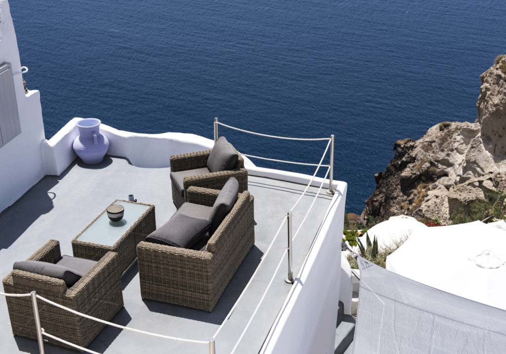 Sitzgruppe auf einer Terrasse eines weissen Hauses auf Santorini mit Blick zum tiefblauen Meer
