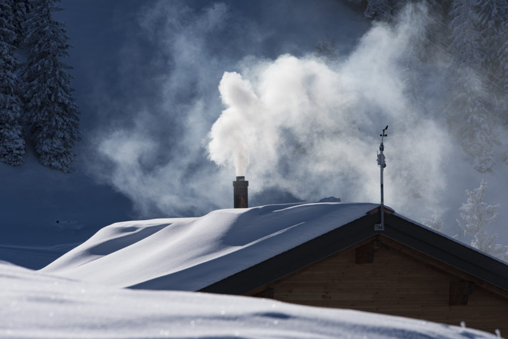 schneebedecktes Hausdach mit qualmendem Kamin im Streiflicht