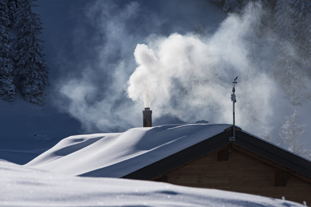 eingeheizt schneebedecktes Hausdach mit qualmendem Kamin im Streiflicht