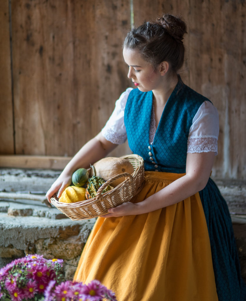 Portrait Fotografie, Available Light: blau-gelbes Dirndl im Halbportrait mit K&uuml;rbiskorb, Seitenlicht, Holzwand