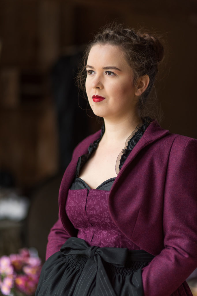 Portrait Fotografie, Available Light: klassisches, dunkelrotes Dirndl mit Cape im Halbportrait seitlich