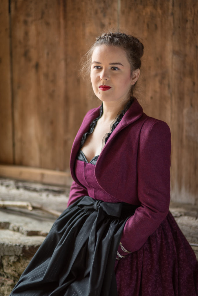 Portrait Fotografie, Available Light: klassisches, dunkelrotes Dirndl mit Cape im Halbportrait seitlich