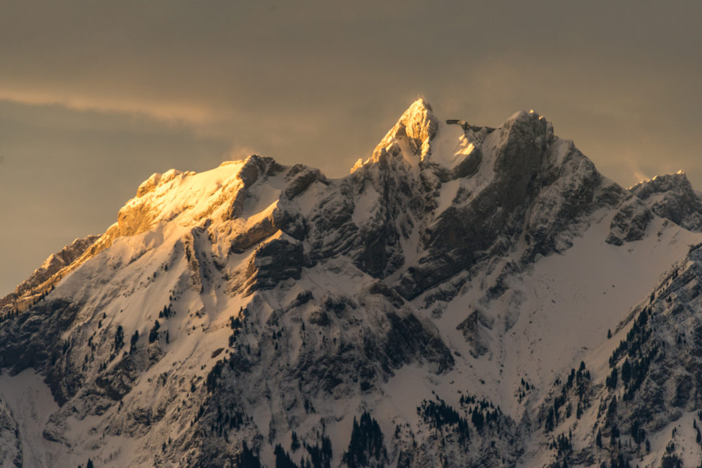 verschneiter Berggipfel mit ersten Sonnenstrahlen und verwehendem Wind