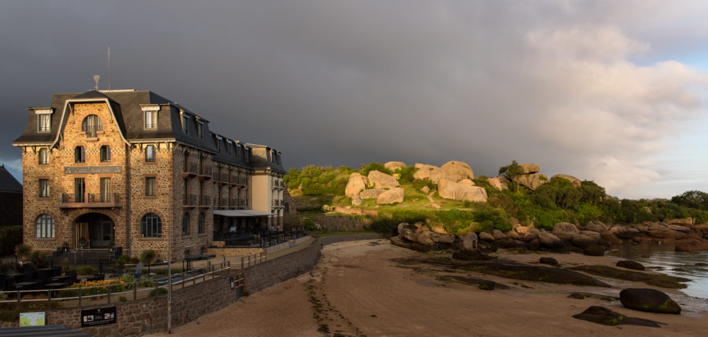 altes Hotel in der Bucht bei Ploumanac'h in den ersten Sonnenstrahlen, im Hintergrund dunkle Wolken