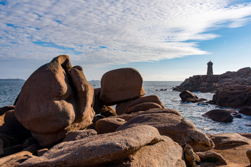 rote Granitbl&ouml;cke an der K&uuml;ste im Hintergrund ein einsamer Leuchtturm