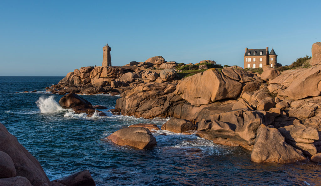 Breizh, Bretagne, Maison du Littoral, einsames Steinhaus und Leuchtturm inmitten roter Granitfelsen am Meer bei Sonnenuntergang