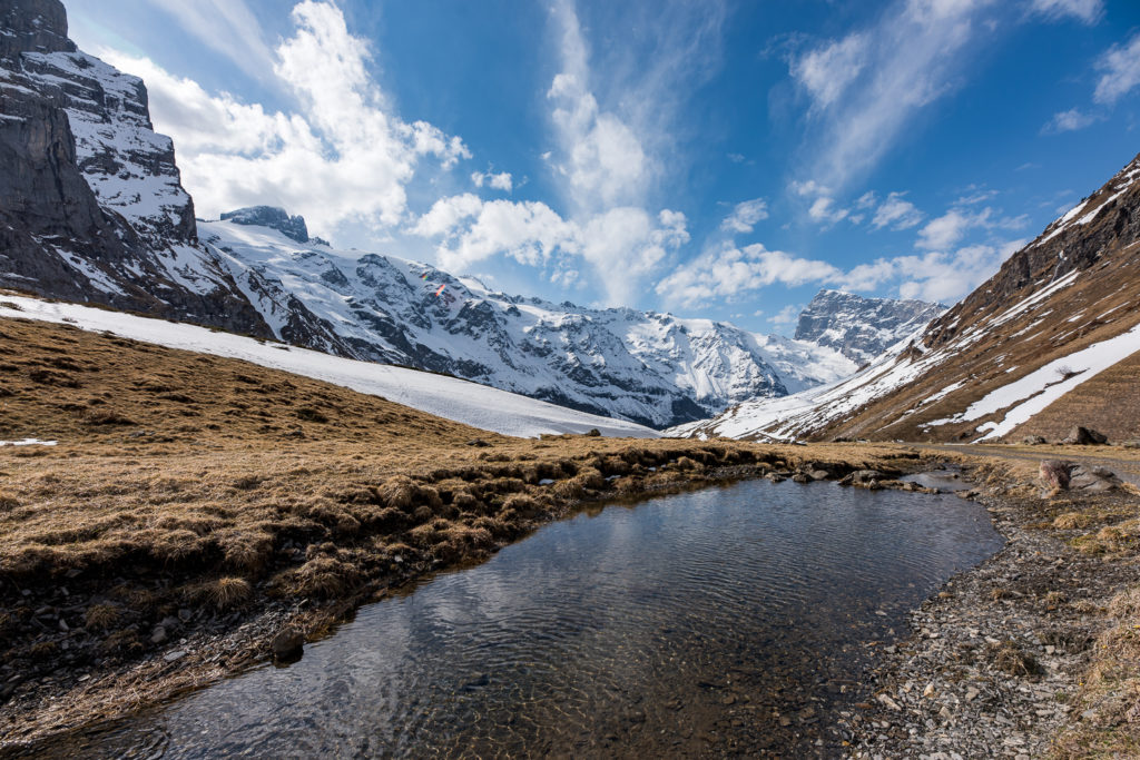 Bergsee im Vordergrund, im Hintergrund verschneite Berggipfel, leicht bew&ouml;lkter Himmel