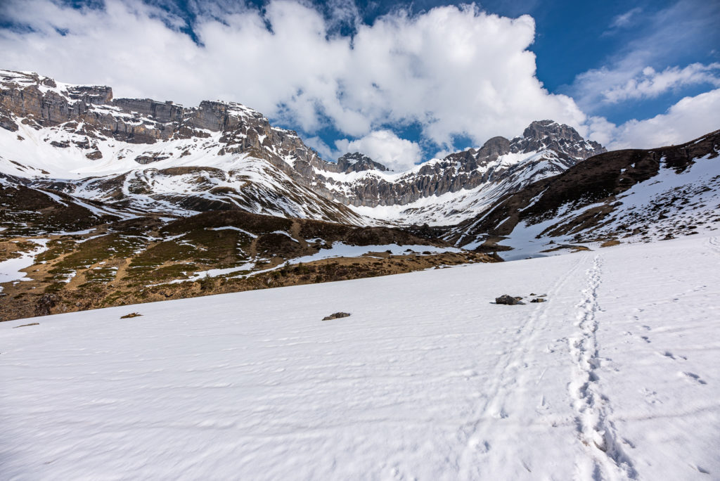 Schneefeld, im Hintergrund verschneite Berggipfel und Wolken am Himmel