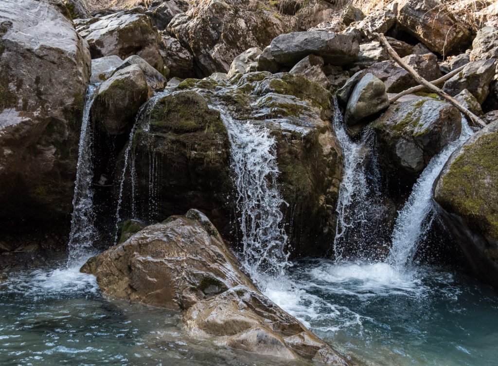 mehrfacher kleiner Wasserfall eines Wildbaches über nassen moosbewachsenen Steinblöcken