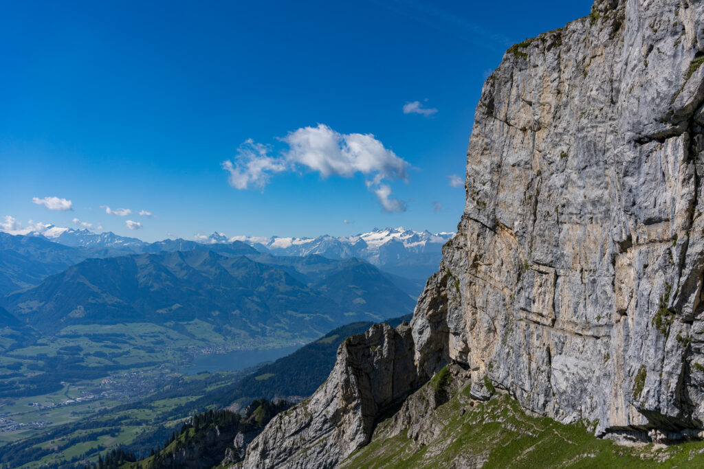 senkrechte Felswand, im Hintergrund Berggipfel der Alpen