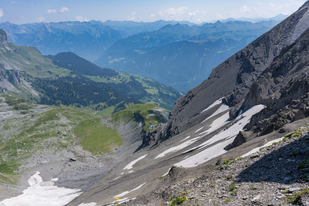 Ausblick über steile Geröllfelder mit Schneeresten, im Hintergrund die Glarner Alpen