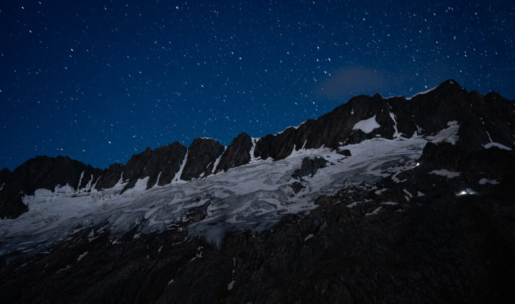 Sternenhimmel über dunklen Berggipfeln und leuchtenden Gletschern