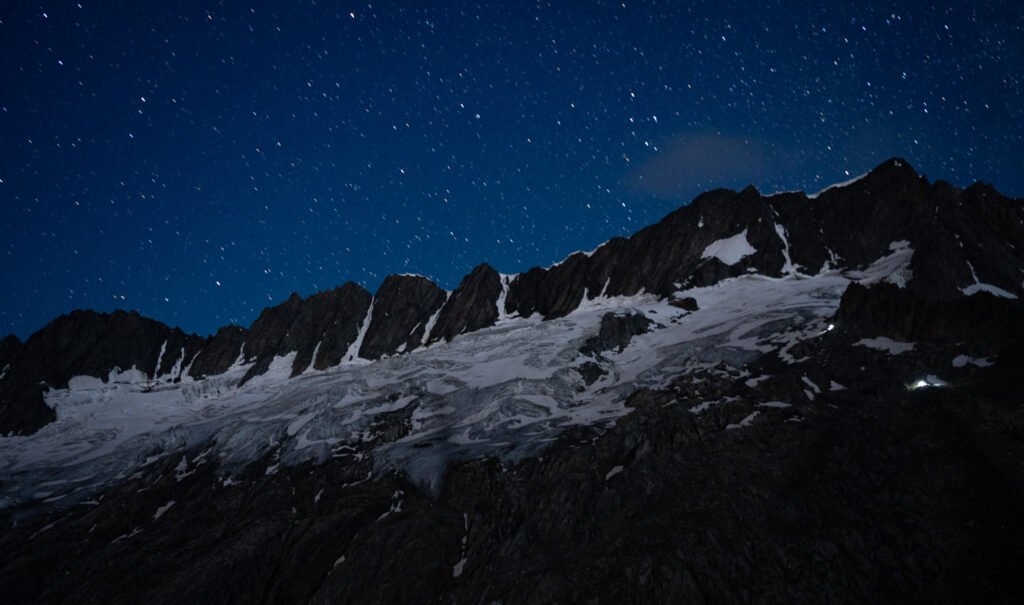 Sternenhimmel &uuml;ber dunklen Berggipfeln und leuchtenden Gletschern