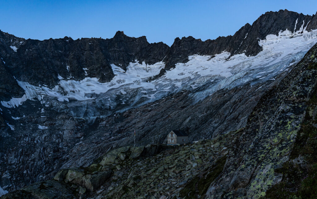 Berghütte, im Hintergrund Gletscher und Berggipfel im Morgengrauen