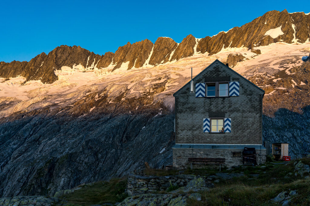 Berghütte mit Berggipfeln und Gletschern in der ersten Morgensonne