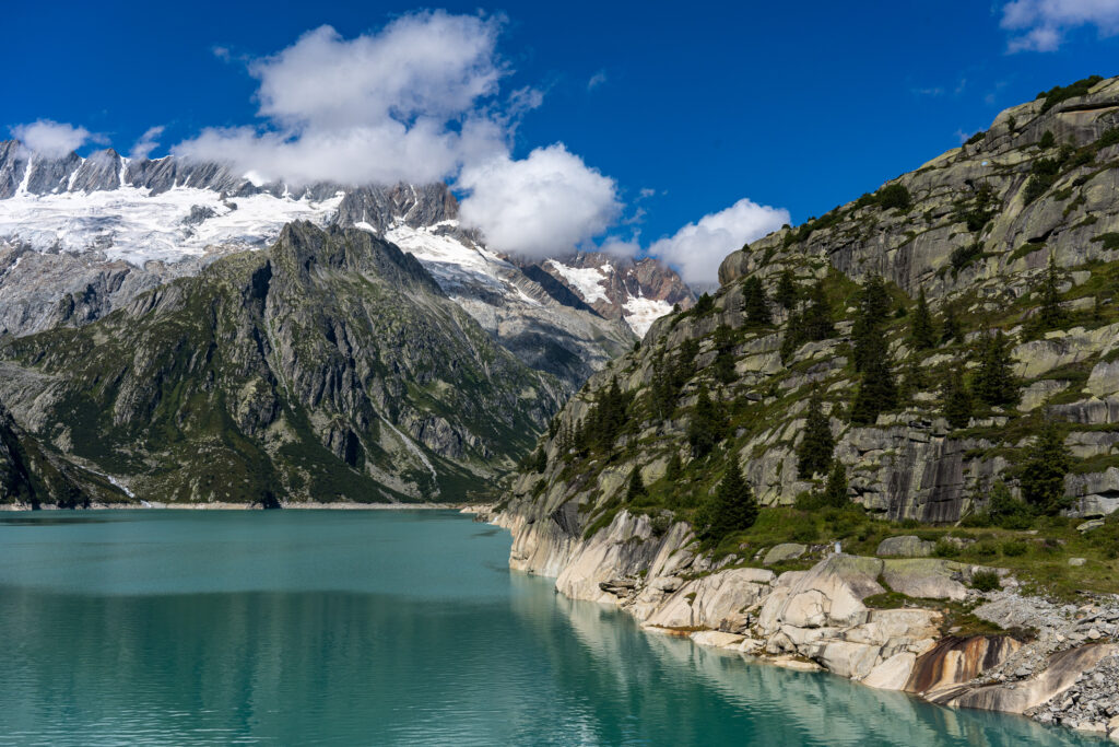t&uuml;rkisblauer Bergsee mit Berggipfeln und Gletschern bei Sonnenlicht und weissen Quellwolken
