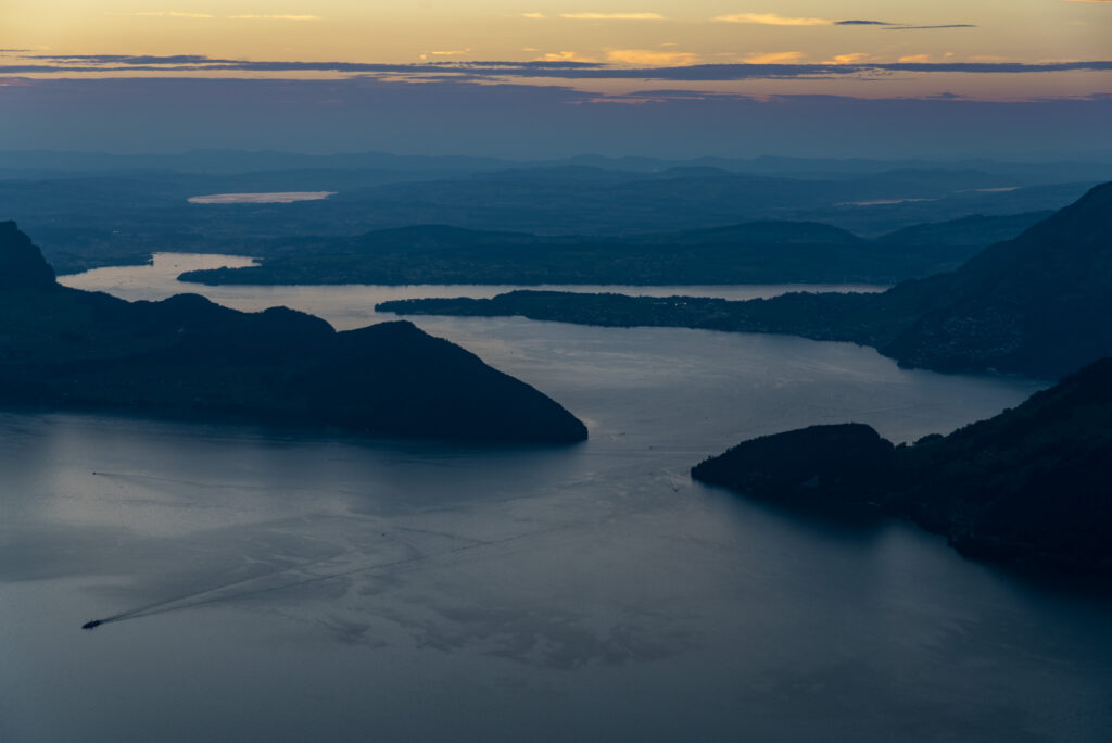 im Abendlicht leuchtender See vor schwarzen Bergsilhouetten